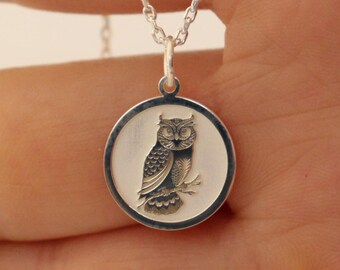 May include: Silver necklace with a round pendant featuring an engraved image of an owl.