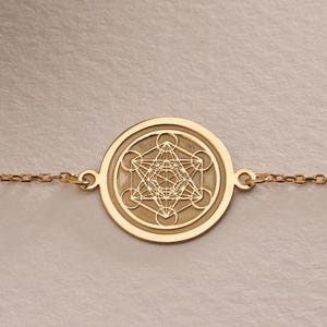 Puede incluir: Un brazalete de cadena dorada con un colgante redondo con un diseño geométrico.