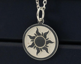 May include: A silver-colored necklace with a circular pendant featuring a sun design. The pendant hangs from a delicate chain. The necklace is displayed on top of a stack of three dark blue boxes.