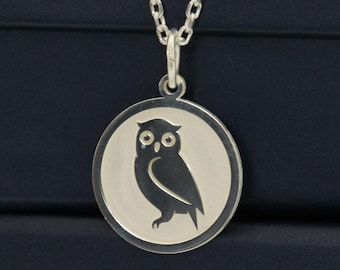 May include: A silver owl pendant necklace with a round charm. The owl is depicted in a silhouette on a white background. The necklace is displayed on top of two dark blue boxes.