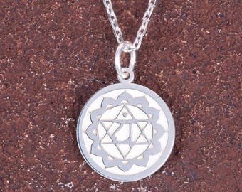 May include: A silver-colored pendant necklace featuring a circular charm with a detailed, symmetrical design. The charm has a central geometric pattern surrounded by a floral-like border. The necklace chain is also silver.