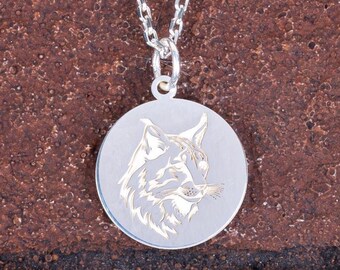 May include: A silver pendant necklace featuring a detailed engraving of a lynx head within a circular frame. The lynx is depicted in profile, showcasing its distinctive ear tufts and facial features. The chain is a delicate silver link design.