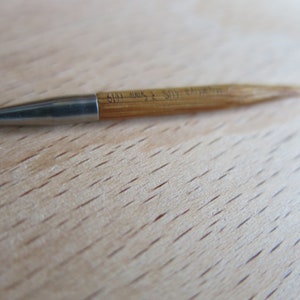 May include: A close-up of a 5.5 mm knitting needle with a green tip and a wooden shaft. The needle is made of metal and has a smooth finish.