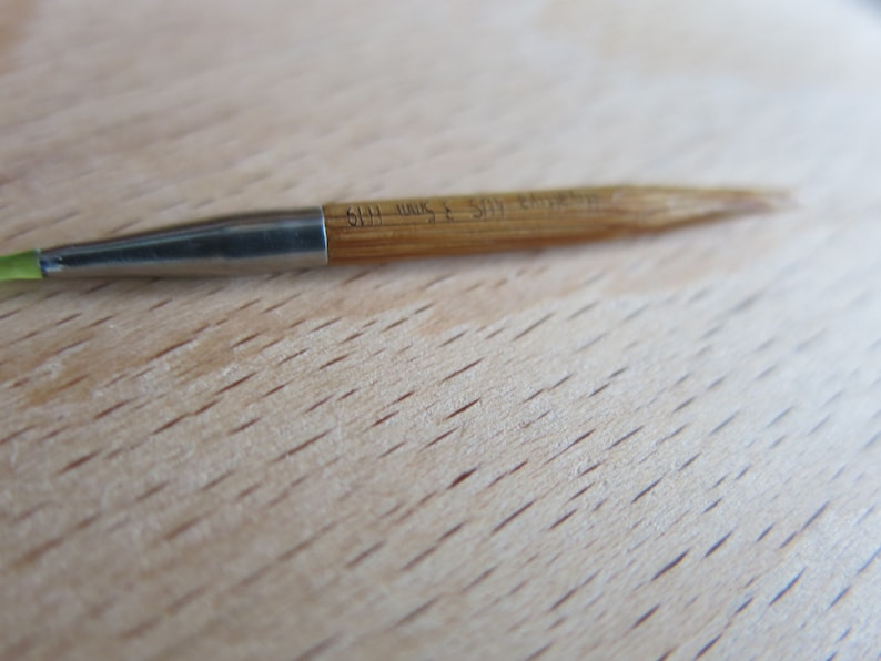 May include: A close-up of a 5.5 mm knitting needle with a green tip and a wooden shaft. The needle is made of metal and has a smooth finish.