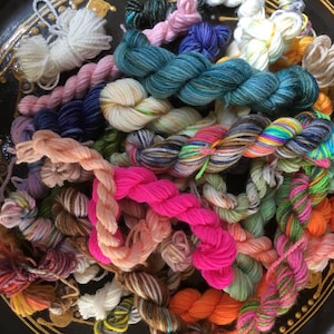 May include: A collection of colourful yarn skeins in various shades of pink, blue, green, orange, white, and brown. The yarn is arranged in a circular pattern on a dark brown surface.