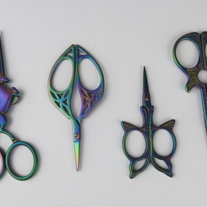 May include: Four decorative scissors with iridescent rainbow finishes. The scissors feature different designs, including a unicorn, a leaf, a butterfly, and a simple design.
