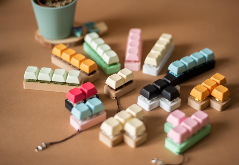 May include: A collection of colorful keycaps in various shapes and sizes. The keycaps are arranged in a circular pattern on a brown surface. The keycaps are made of plastic and have a variety of colors, including green, blue, pink, orange, and white.