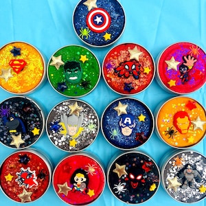 May include: A selection of round containers filled with glittery slime in various colours, each adorned with a superhero emblem and star-shaped decorations. The containers feature characters such as American superhero and Web-crawler.