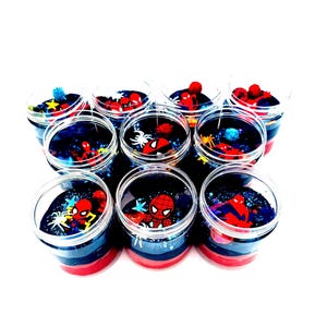 Op de afbeelding: Een verzameling doorzichtige plastic potten gevuld met kleurrijke slijm. Elke pot heeft een Spiderman-afbeelding en glitter. Het slijm is gelaagd met rode, blauwe en zwarte kleuren. De potten zijn in een cirkel gerangschikt.