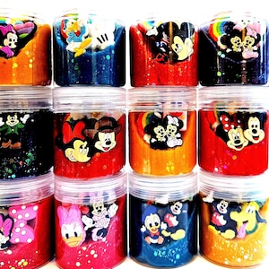 May include: A selection of clear plastic jars filled with colourful slime. Each jar features a different Disney character, including Mickey Mouse, Minnie Mouse, and Donald Duck. The slime is various colours, including red, blue, and orange, with glitter.
