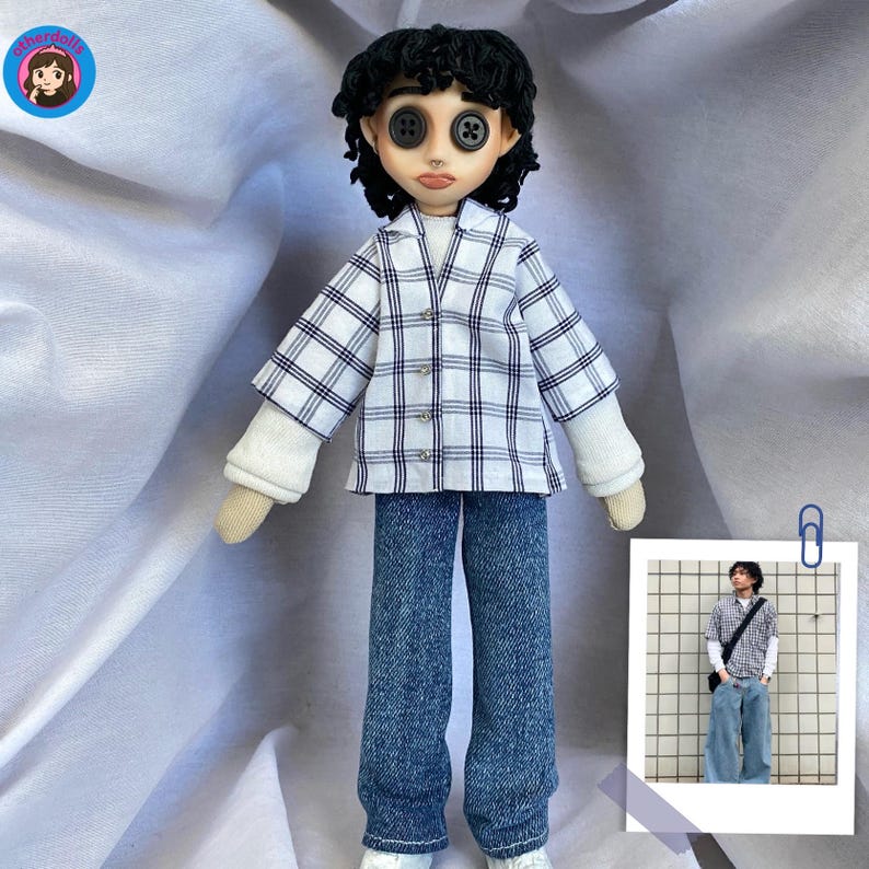 Puede incluir: Una mu&ntilde;eca hecha a mano con ojos de bot&oacute;n, vestida con una camisa a cuadros blanca y azul sobre una camiseta blanca de manga larga y vaqueros azules. La mu&ntilde;eca tiene el pelo rizado negro y zapatillas blancas. Se adjunta una imagen m&aacute;s peque&ntilde;a de una persona con ropa similar.