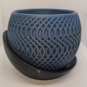 May include: A blue ceramic planter with a wavy pattern, sitting on a black saucer.