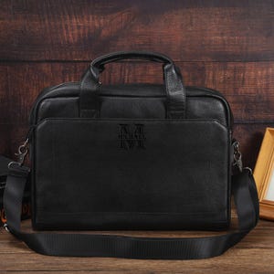 May include: Black leather briefcase with a top handle and a detachable shoulder strap. The front of the bag features the embossed text "MICHAEL". The bag has a zippered main compartment and a front pocket.
