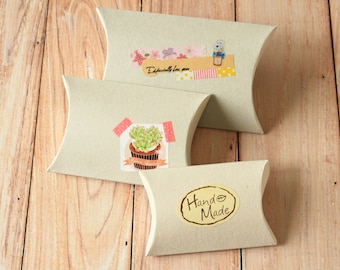 May include: Three brown pillow boxes with decorative paper tape and stickers. The top box has a sticker with the text "Especially for you". The middle box has a sticker with a potted succulent. The bottom box has a sticker with the text "Hand Made".