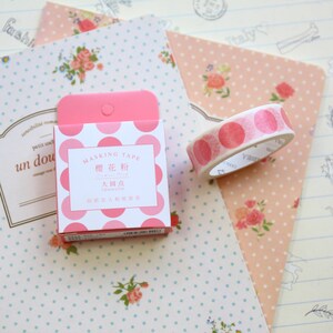May include: A pink and white polka dot washi tape dispenser with the text "Masking Tape" and "樱花" in Japanese. The dispenser is sitting on a pink and white polka dot background.