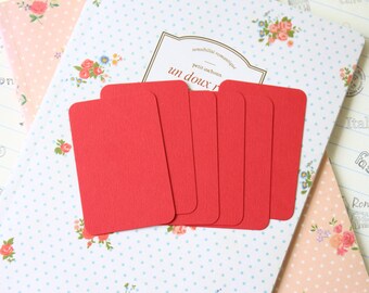May include: Six red rectangular gift tags with rounded corners, arranged in a row on a white background with a blue polka dot pattern and pink floral designs. The text "un doux" is visible on the background.