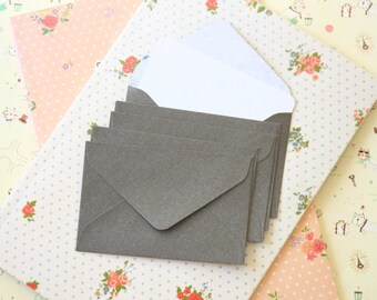 May include: A stack of six gray envelopes on a patterned background. The envelopes are all the same size and have a simple, elegant design.