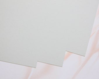 May include: Two sheets of light grey cardstock paper, stacked on top of each other, with the top sheet slightly overlapping the bottom sheet. The paper is smooth and has a subtle texture.