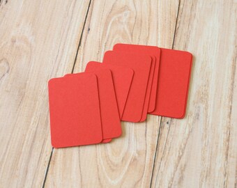 May include: A stack of six red blank cards on a wooden surface.