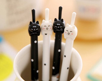 May include: Four cat-themed pens in a white ceramic cup. Two pens are black with white polka dots, and two are white with black polka dots. Each pen has a cat-shaped top with a smiling face. The pens are a fun and cute stationery item.