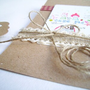 May include: A brown paper card with a white lace trim and twine tied around it. The card has a hand-drawn illustration of two cartoon characters with the text "Take a Pic" on it.