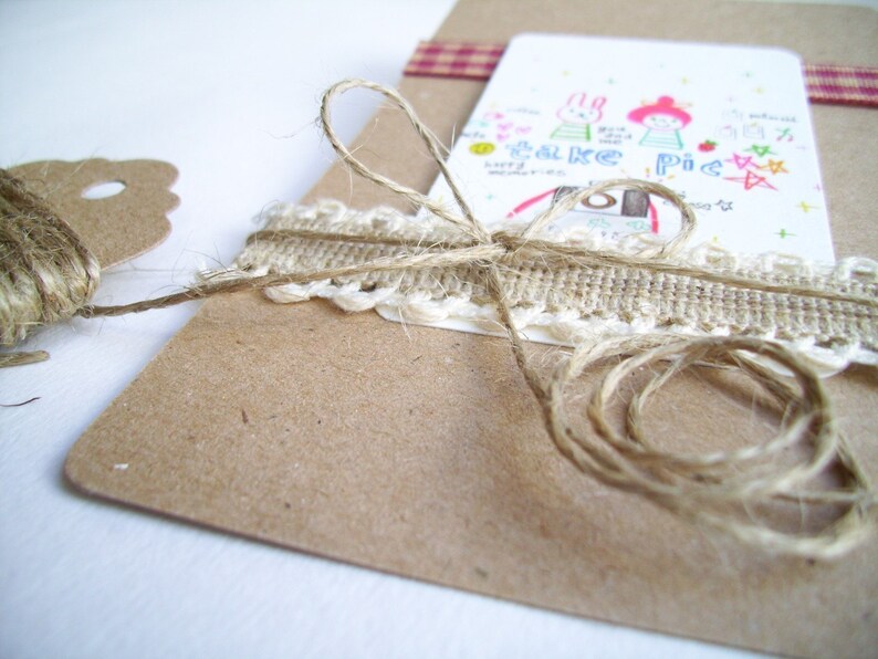 May include: A brown paper card with a white lace trim and twine tied around it. The card has a hand-drawn illustration of two cartoon characters with the text "Take a Pic" on it.