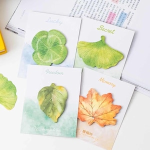 May include: Four rectangular cards featuring leaf-shaped sticky notes. The cards are labelled Lucky with a green clover, Secret with a green ginkgo leaf, Freedom with a green leaf, and Memory with an orange maple leaf. Each card has a watercolour background.