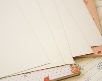 May include: A stack of blank white cards on top of a notebook with a floral pattern. The notebook has a light blue background with white polka dots and pink flowers.