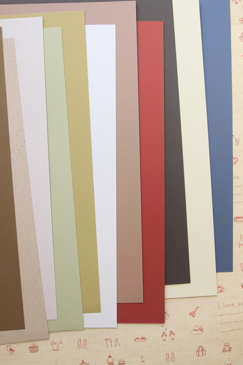 Puede incluir: Una colecci&oacute;n de 10 hojas de papel de diferentes colores, cada una con una textura &uacute;nica. Las hojas de papel est&aacute;n dispuestas en una pila vertical, con la hoja superior de color marr&oacute;n claro y la hoja inferior de color azul oscuro.
