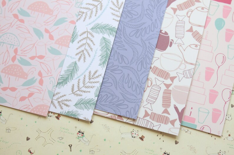 May include: Five different patterned sheets of paper. The patterns include pink and green mushrooms, brown and green leaves, blue leaves, pink and brown candy, and pink and blue balloons and cups.