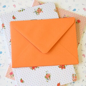 May include: A stack of three envelopes with a floral pattern. The top envelope is orange and the bottom two envelopes are white with blue polka dots and small floral designs.