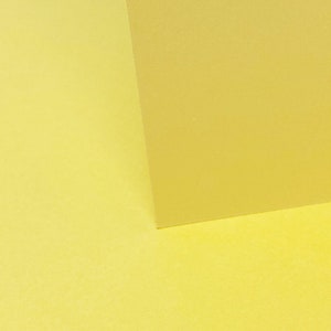 May include: Two pieces of yellow paper, one on top of the other, creating a diagonal line.