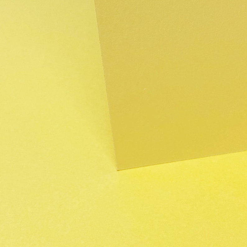 May include: Two pieces of yellow paper, one on top of the other, creating a diagonal line.