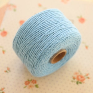 May include: A spool of light blue cotton twine. The twine is wound tightly around a cardboard core.