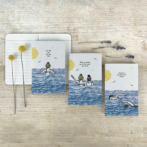 May include: Three illustrated greeting cards with ocean-themed designs. The cards feature swimmers, waves, and the sun, with text that reads "Let the sea set you free", "When in doubt go to the water and swim", and "Ocean is my favourite colour".
