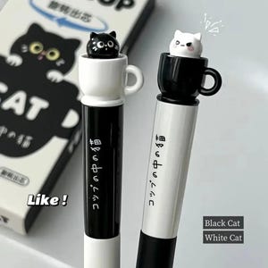 以下が含まれることがあります： 黒と白の2本のペン。それぞれカップに入った猫のミニチュアフィギュアが上に乗っています。黒いペンは白いカップ、白いペンは黒いカップです。ペンには日本語のテキストが印刷されています。