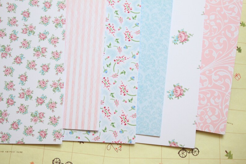 May include: A set of six patterned paper sheets in pink, blue, and white. The patterns include floral designs, stripes, and swirls.