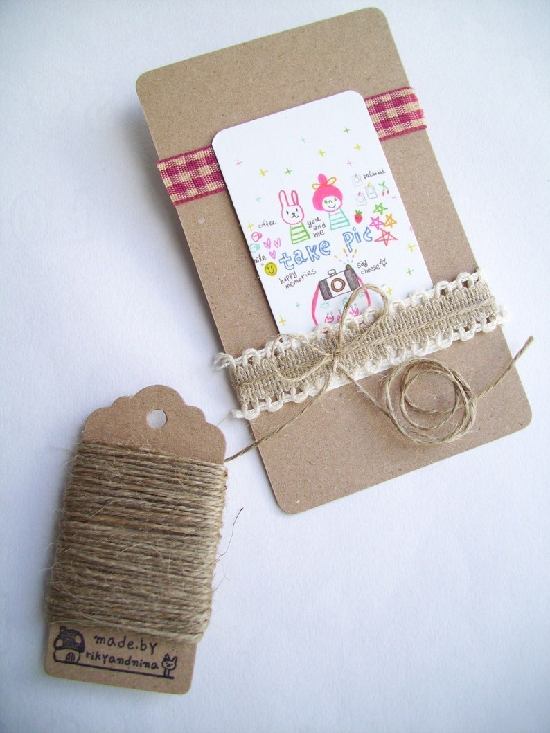 May include: A brown card with a white card attached to it. The white card has a drawing of two cartoon characters with the text "take pic" and other text. The card is tied with a brown twine and a white lace ribbon. A brown tag with twine is in the lower left corner of the image.