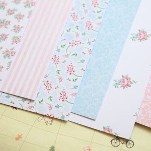 May include: Assortment of patterned paper sheets in pink, blue, and white with floral and geometric designs.