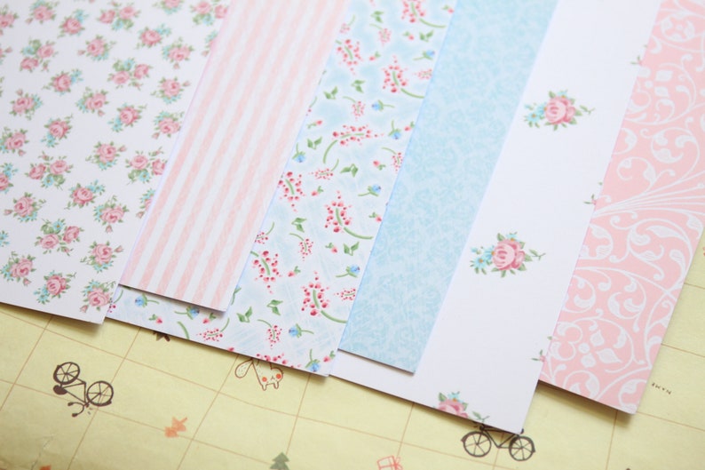 May include: Assortment of patterned paper sheets in pink, blue, and white with floral and geometric designs.