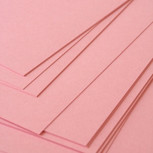 May include: Stack of pink paper sheets, layered and overlapping, creating a textured background.