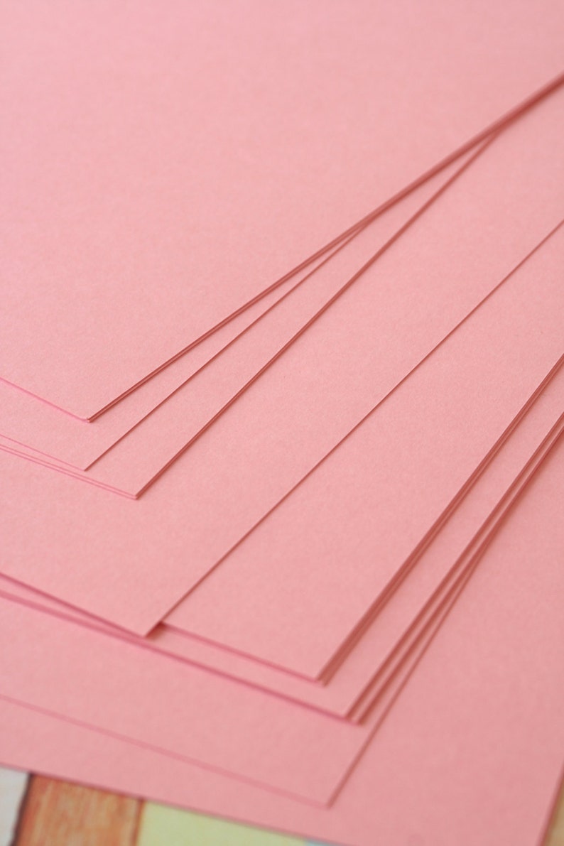 May include: Stack of pink paper sheets, layered and overlapping, creating a textured background.