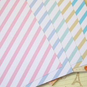 May include: Five sheets of patterned paper with diagonal stripes. The paper is in shades of pink, blue, light blue, and beige.