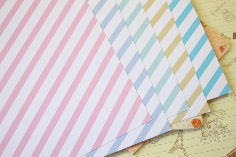 May include: Five sheets of patterned paper with diagonal stripes. The paper is in shades of pink, blue, light blue, and beige.