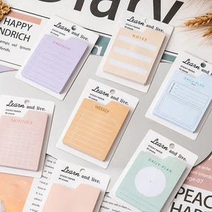 May include: A collection of seven rectangular sticky note pads in pastel colors, each mounted on a white card labeled Learn and live. The pads feature printed templates including checklist, notes, daily plan, monthly, and weekly layouts.