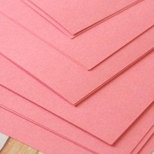 May include: Stack of pink construction paper. The paper is folded in a fan shape, creating a geometric pattern.