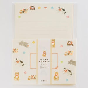 May include: A stationery set featuring cream-colored paper with illustrations of cats wearing red ribbons. The packaging includes a central band with the text "ハンコのレターセット" and "ねこと絆" alongside small cat graphics and a "10 5" notation.
