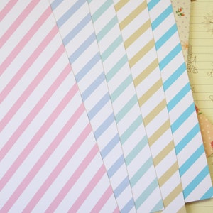 May include: Five sheets of striped paper in pink, light blue, teal, beige, and light blue. The paper is arranged in a fan shape with the pink sheet on top.