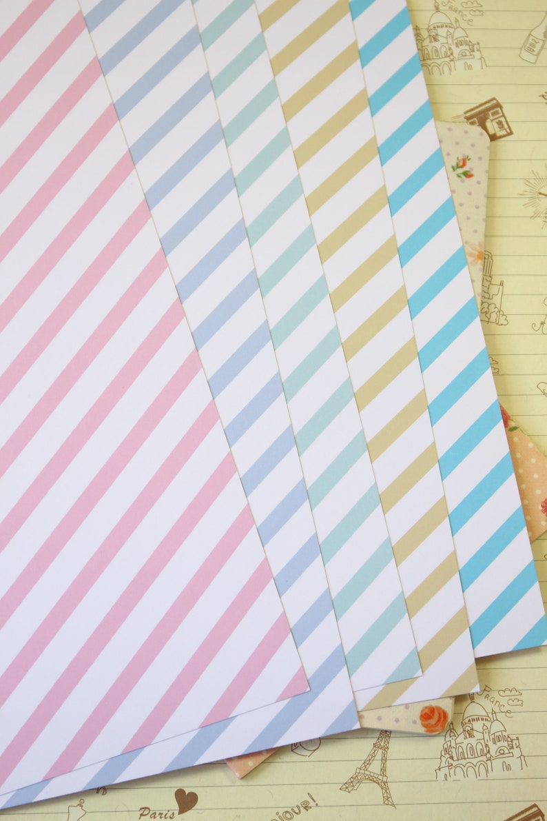 May include: Five sheets of striped paper in pink, light blue, teal, beige, and light blue. The paper is arranged in a fan shape with the pink sheet on top.