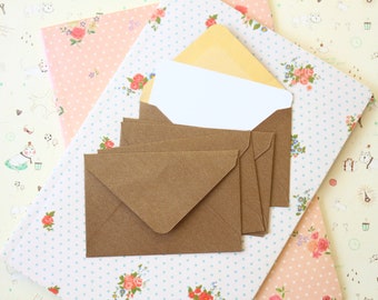 May include: A stack of brown envelopes with a white envelope on top. The envelopes are on a patterned background with pink and blue flowers.